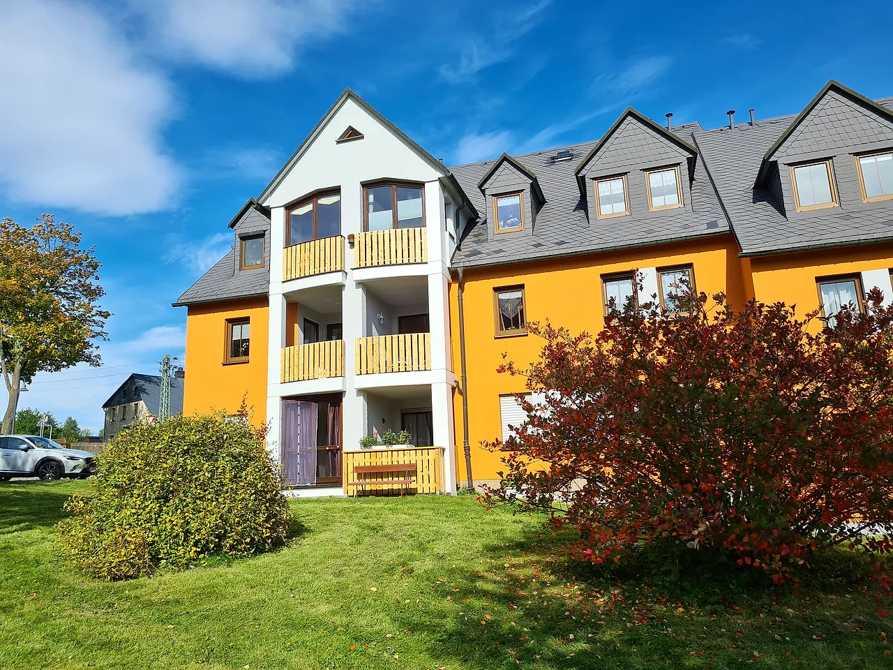 Das Haus mit der Ferienwohnung: orange Fassade, Holzbalkone und Garten im Herbst