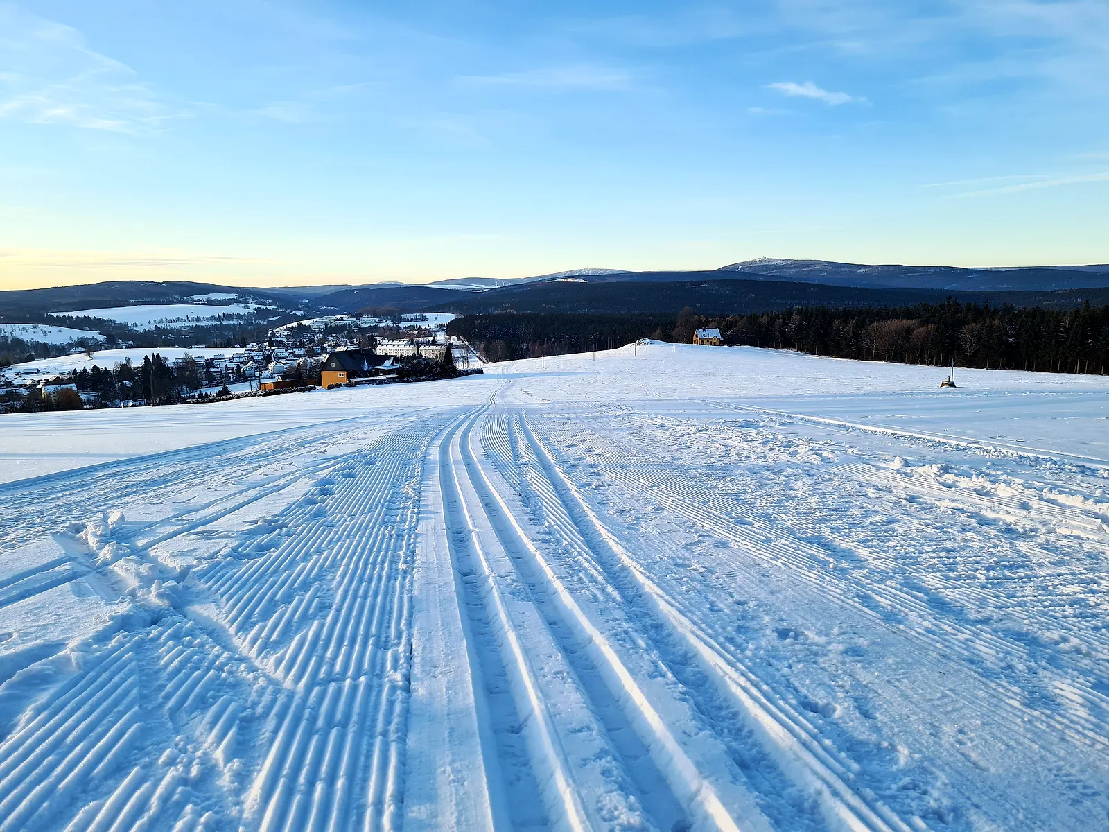 Frisch gespurte Loipe führt über verschneite Felder auf den Ort Bärenstein zu, dahinter die Berge des Erzgebirges